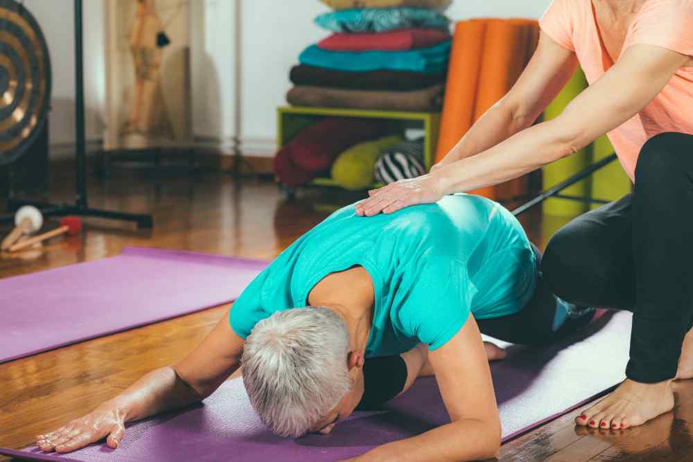 Newtown Therapy | Woman in yoga pose being adjusted by yoga instructor
